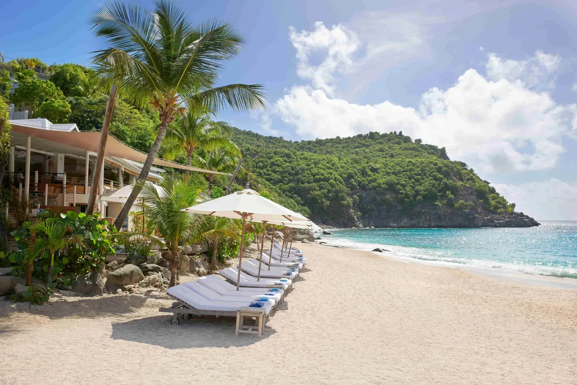 Transats et parasols sur le sable d’un beach club de Saint-Barth, un restaurant de plage parmi les palmiers