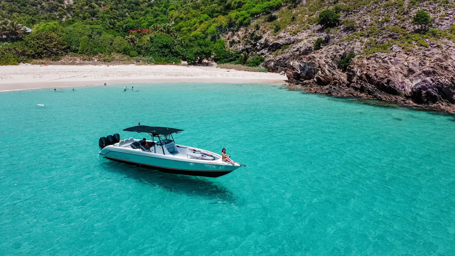 A motorboat anchored in a clear turquoise cove off St Barts, a guest relaxing on the bow