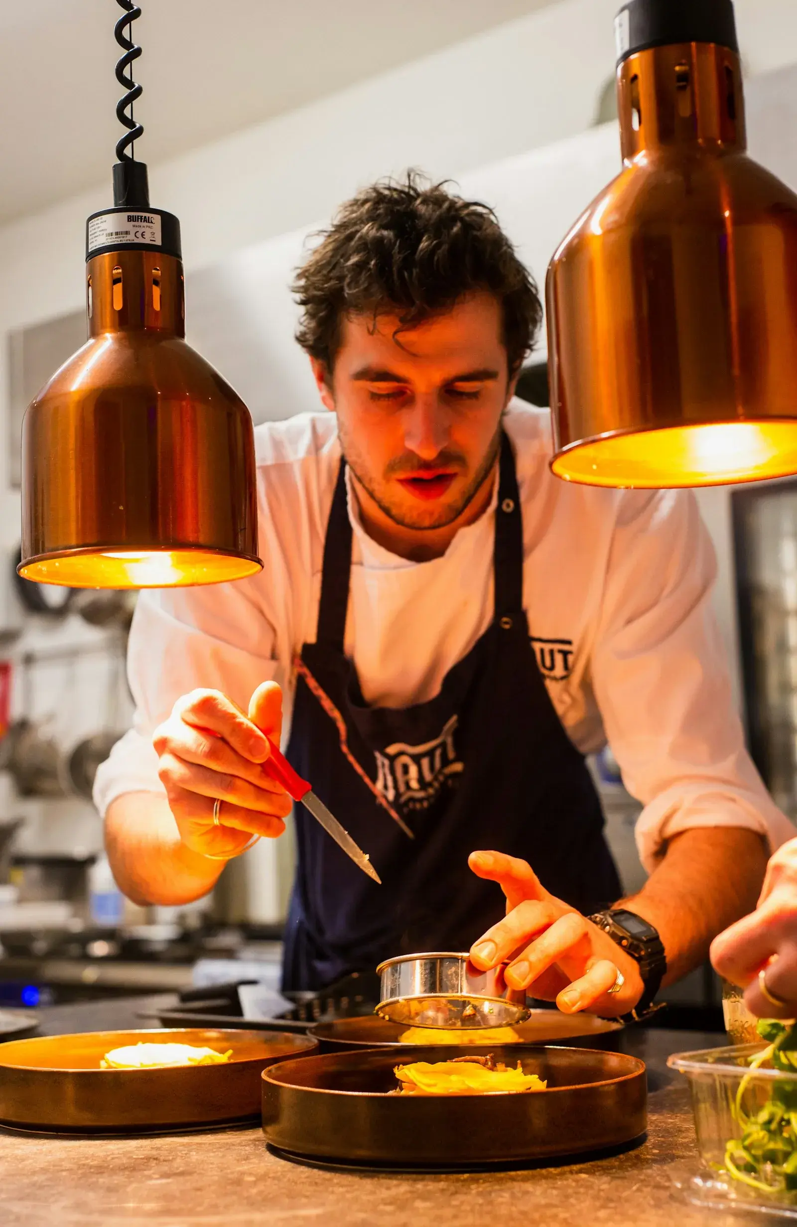 A private chef plating a dish under warm copper heat lamps in a St Barts villa kitchen