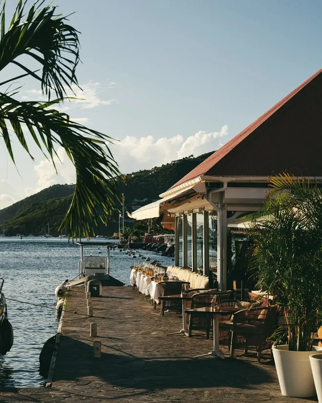A waterfront restaurant terrace on the jetty in Gustavia harbour, St Barts, tables set at golden hour