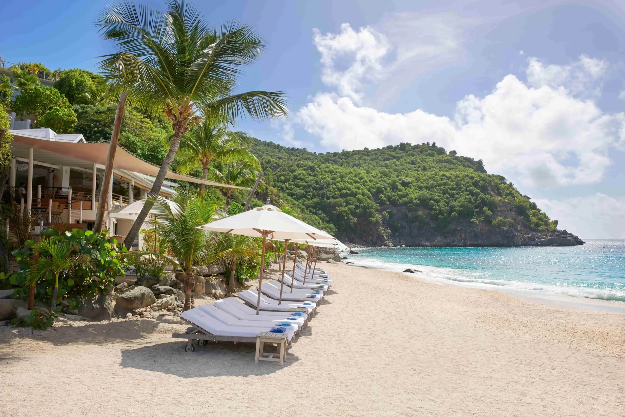 Un beach club tranquille de Saint-Barth, transats sur le sable au bord d’une eau turquoise et claire.