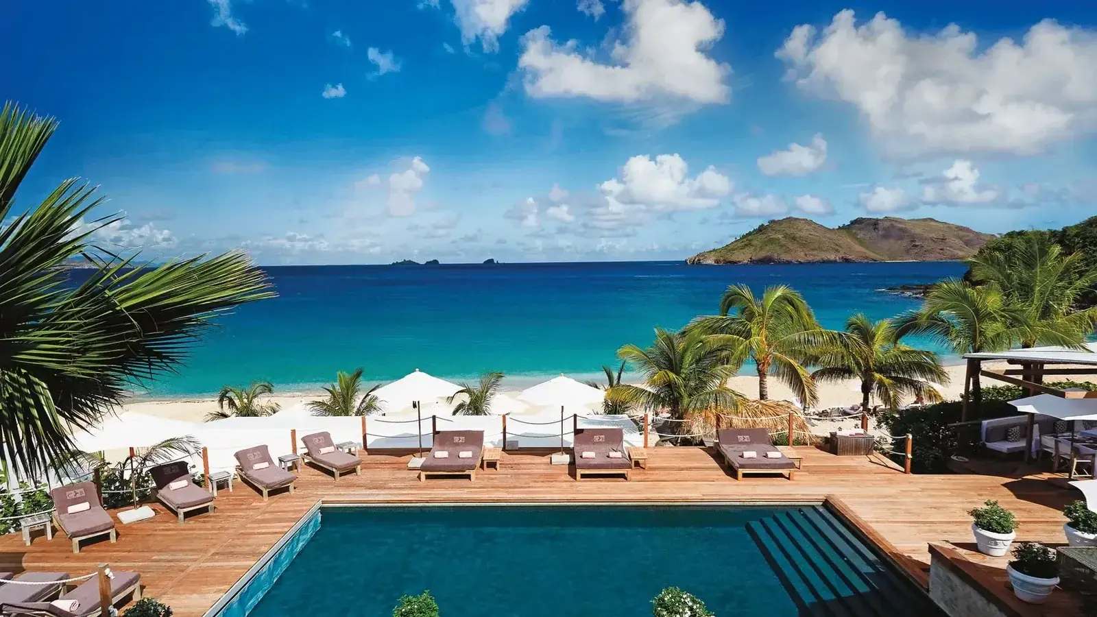 A beachfront hotel pool lined with loungers, palms and islets beyond