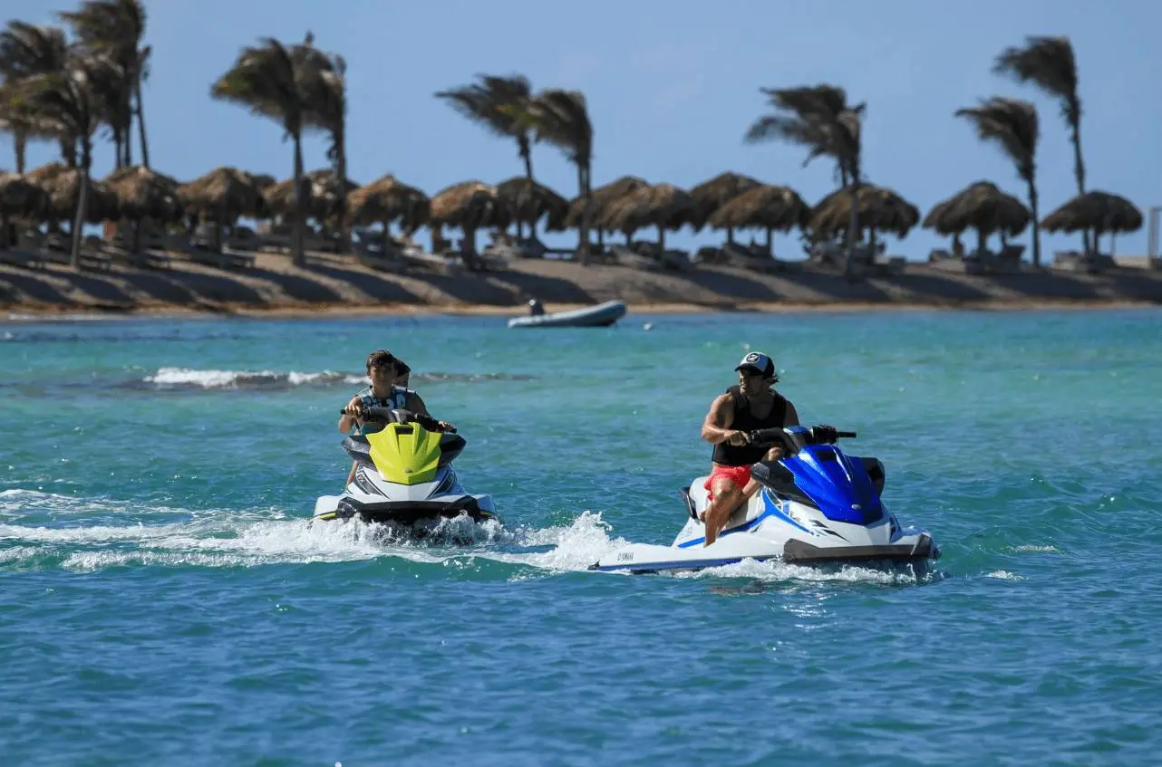 Two jet skis crossing the turquoise water off a St Barts beach lined with sun umbrellas
