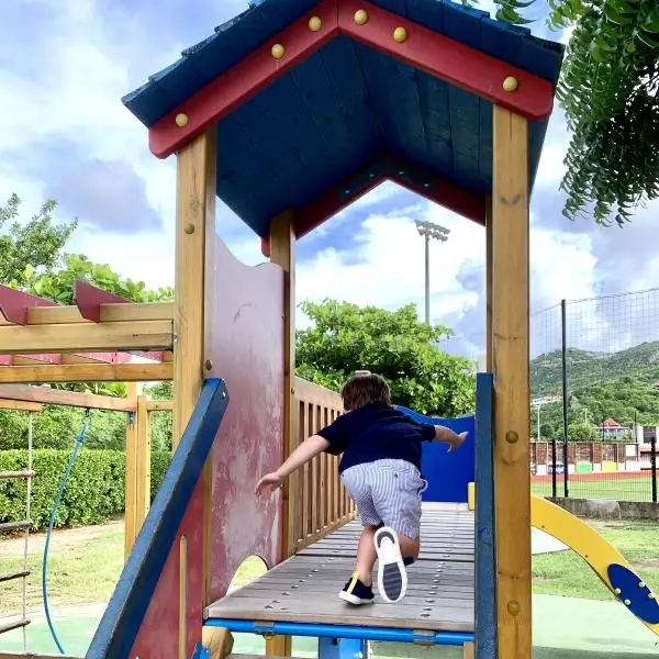 Un jeune enfant sur une aire de jeux en bois à Saint-Barth, les collines vertes derrière