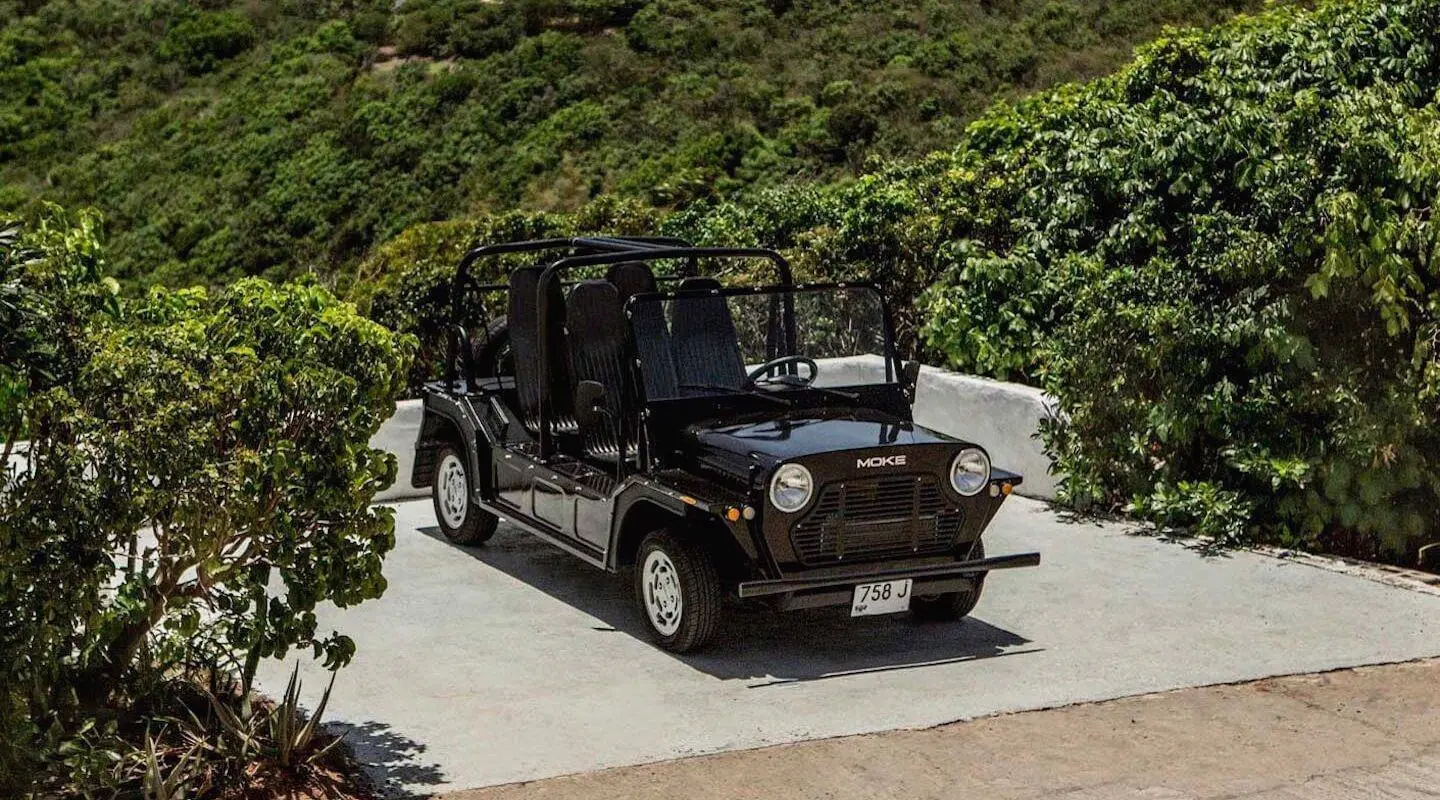 A black Mini Moke parked by the roadside under the trees