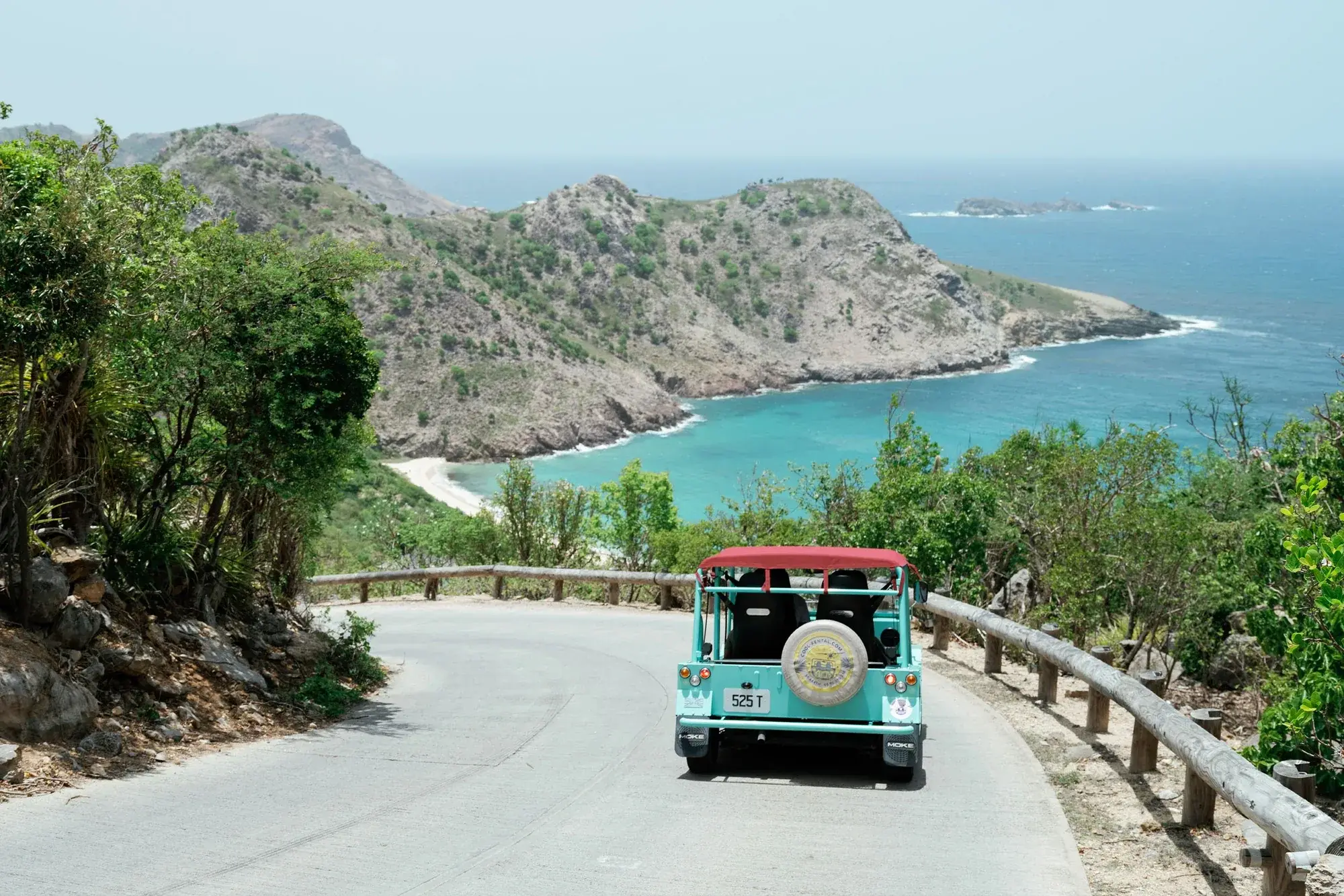 A Mini Moke taking a hairpin bend on a narrow road above a bay