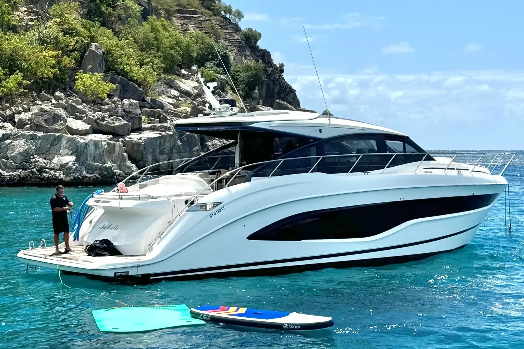A motor yacht at anchor below the rocks, paddleboards floating alongside