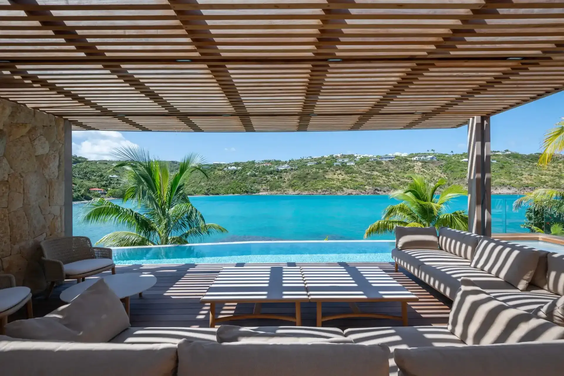 A shaded pergola with deep sofas above a calm turquoise lagoon