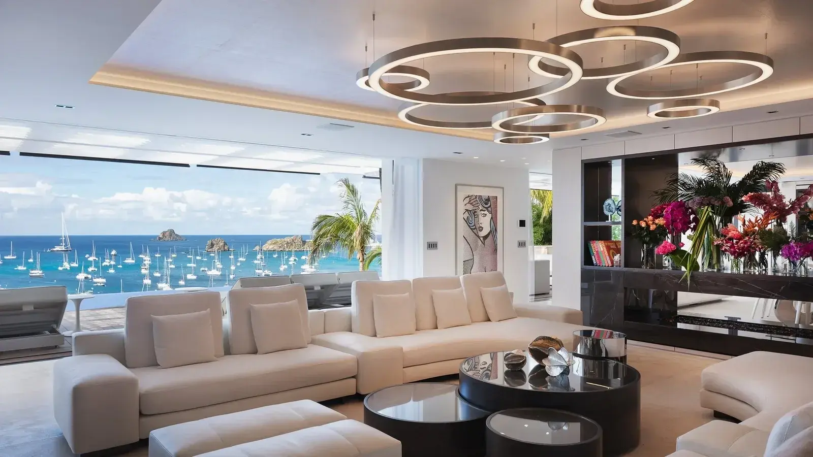 A villa living room set with fresh flowers, sailboats in the bay behind the glass