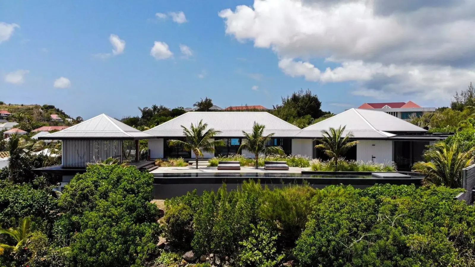 A villa with white roofs and its pool in the greenery, seen from the air